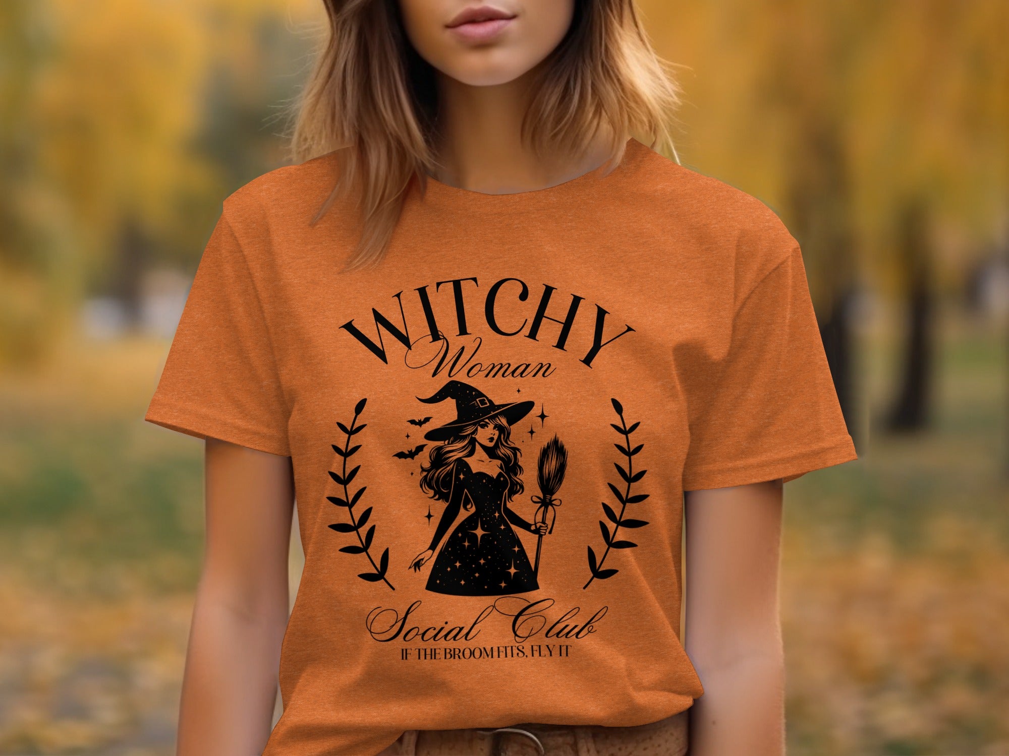 Orange t-shirt with black "Witchy Woman Social Club" graphic featuring a witch and broom.