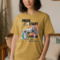 Gold t-shirt with "PRESS START HAVE SOME FUN! LEVEL UP" and game controller graphic.