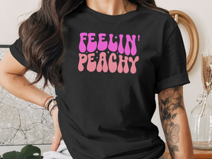 Black t-shirt with pink and light pink "Feelin' Peachy" text and sparkling stars.