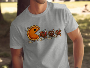 A pie character chases running turkeys on a grey t-shirt.