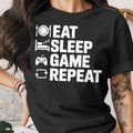 Black t-shirt with white text "Eat Sleep Game Repeat" and icons of a plate, bed, controller, and refresh symbol.