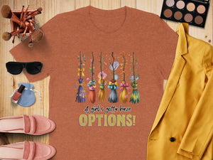 Orange t-shirt with decorative brooms and text "A girl's gotta have OPTIONS!".