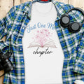 White t-shirt with blue text "Just One More Chapter" and pink floral design.