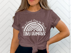 Brown t-shirt with white text "It's a Good Day to Teach TINY HUMANS" and rainbow graphic.