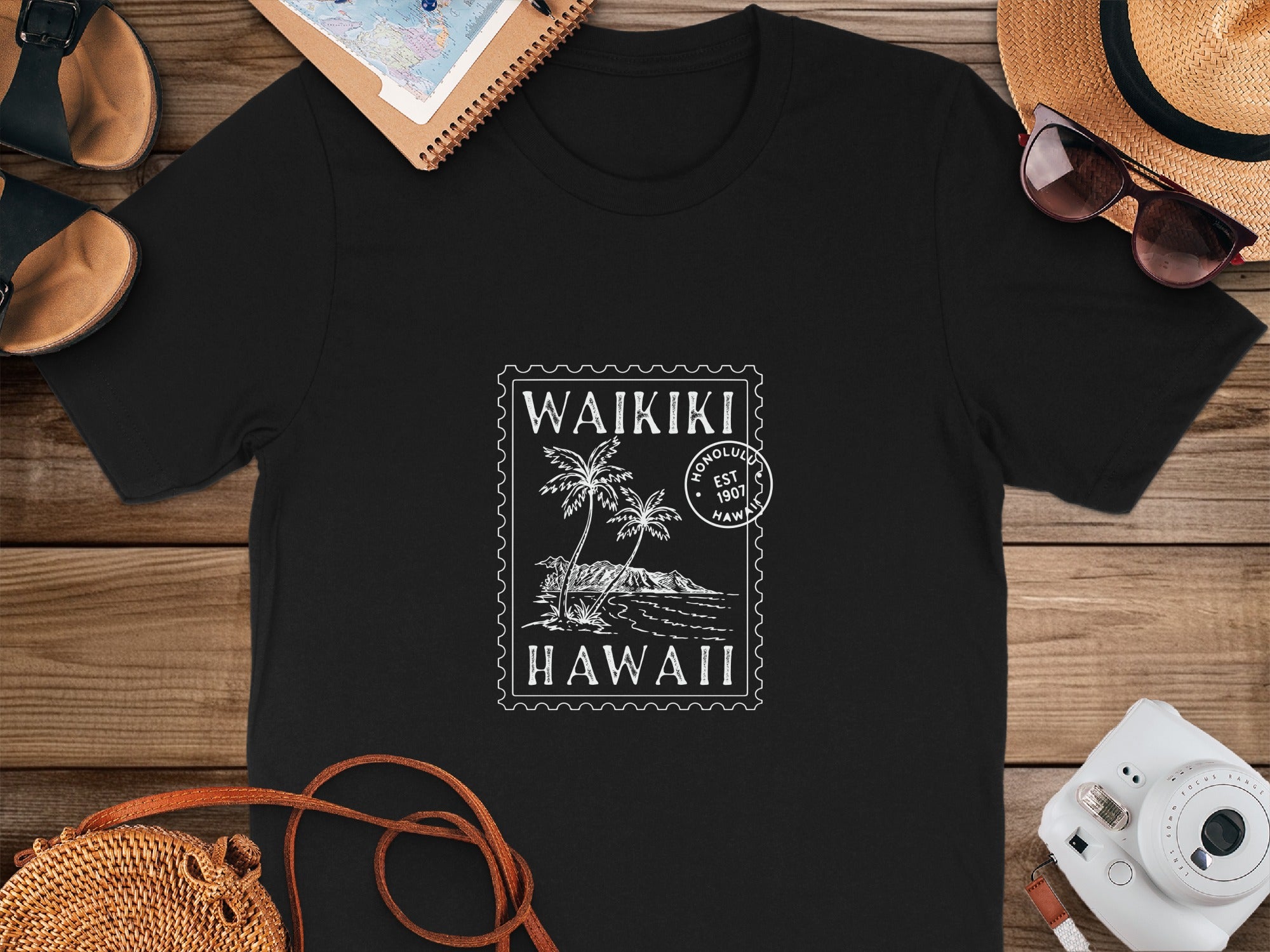 Black t-shirt with white Waikiki Hawaii stamp graphic featuring palm trees and mountains.