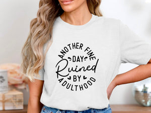 White t-shirt with black text that reads "Another Fine Day Ruined By Adulthood."