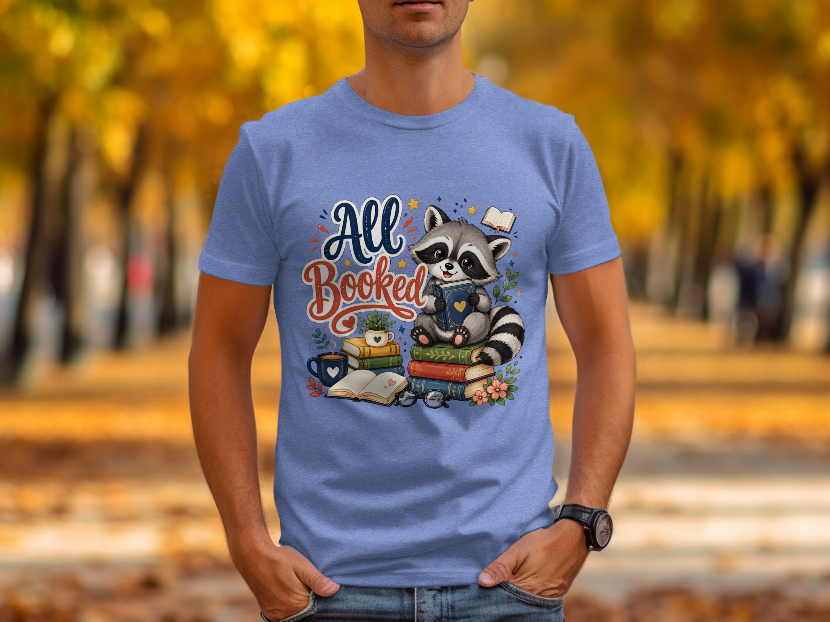 Blue t-shirt featuring a raccoon sitting on books with text "All Booked".