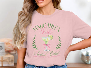 A woman wearing a pink t-shirt with a margarita graphic and text reading Margarita Girls Social Club.
