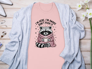 Pink t-shirt with raccoon graphic and text "I'M HERE, I'M AWAKE DON'T PUSH IT."