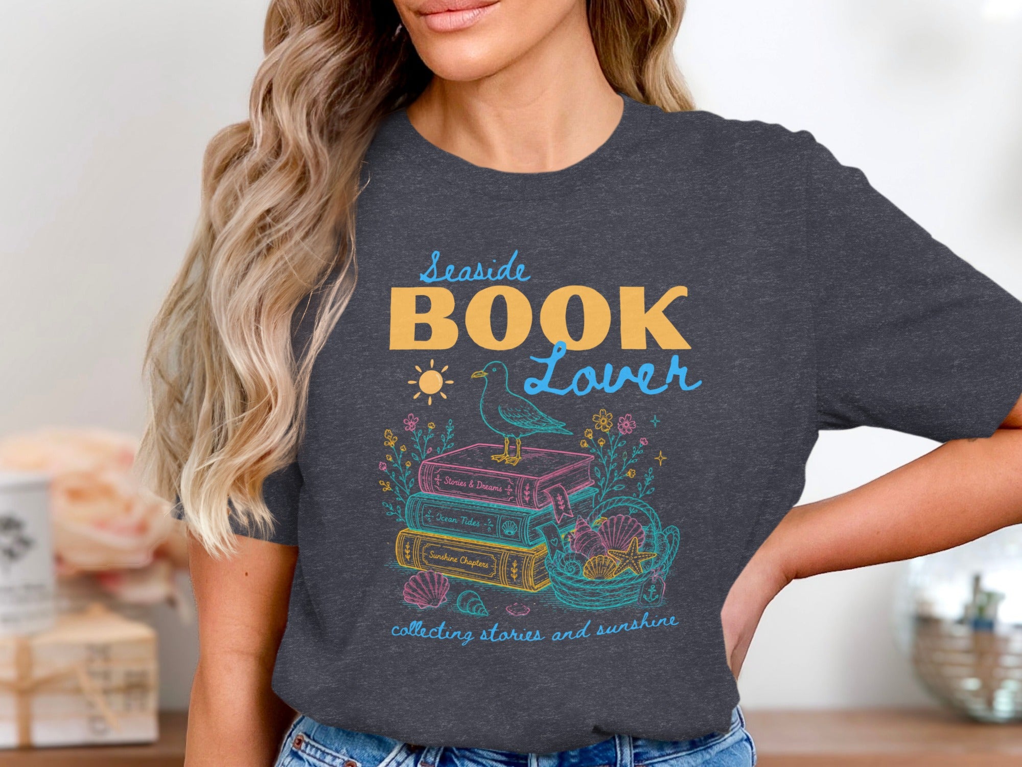 Seaside Book Lover tee with stack of books, seagull, shells, and sun.