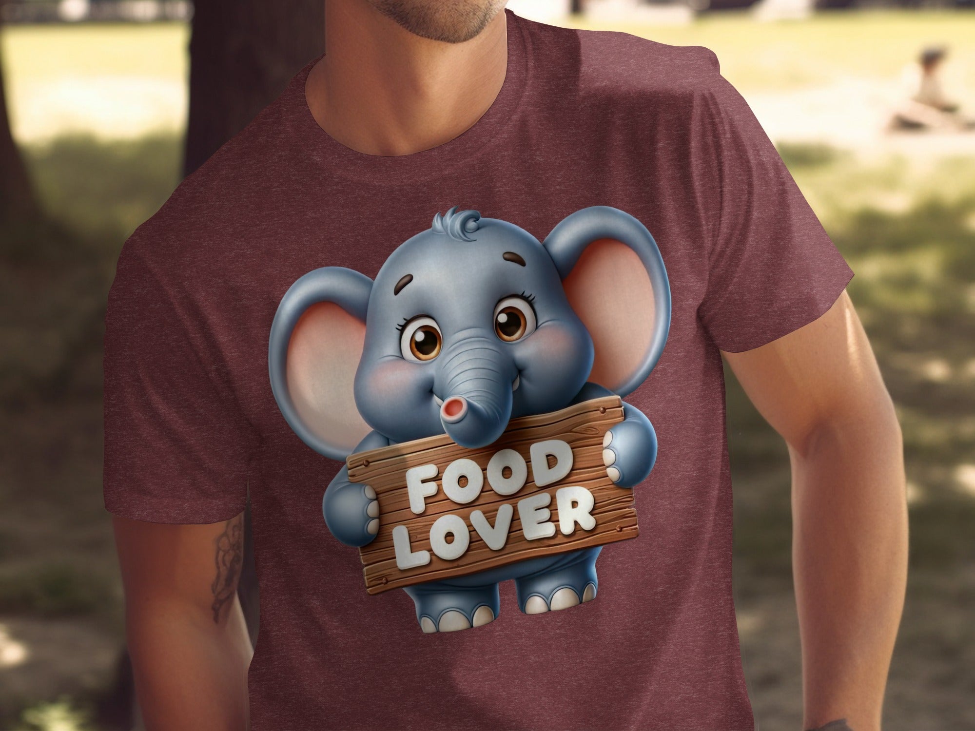 Cartoon elephant with "FOOD LOVER" text on a wooden sign on a maroon t-shirt.