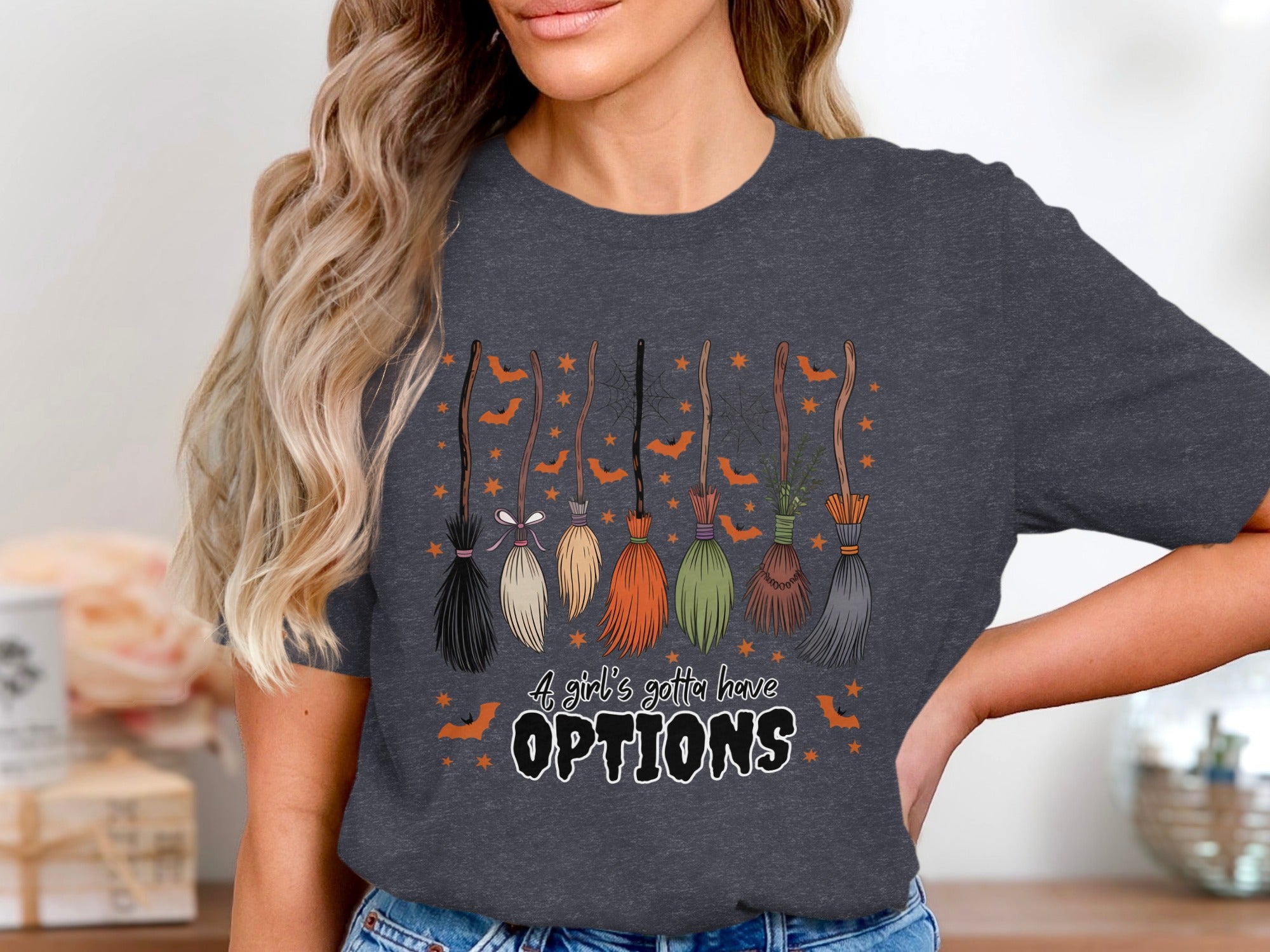 Dark grey t-shirt with a Halloween graphic of brooms, bats, and stars that says "A girl's gotta have OPTIONS".
