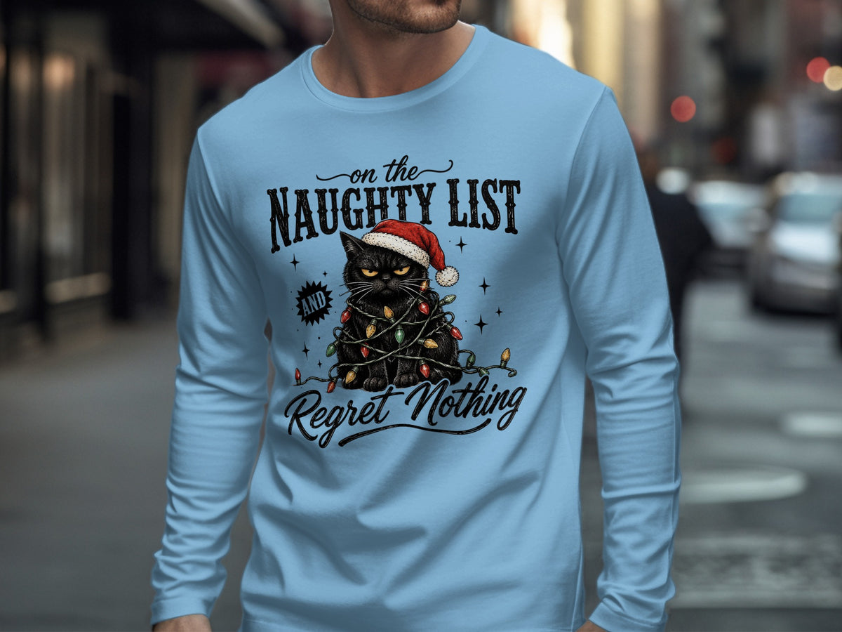 A light blue long-sleeve t-shirt features a graphic of a disgruntled black cat wearing a Santa hat and tangled in Christmas lights, with the text "on the NAUGHTY LIST and Regret Nothing."