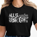 Black t-shirt with white distressed text reading "ALL IS calm ALL IS BRIGHT" and a candle graphic.