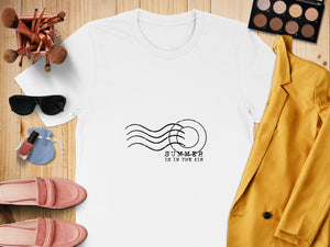White t-shirt with black "SUMMER IS IN THE AIR" graphic.