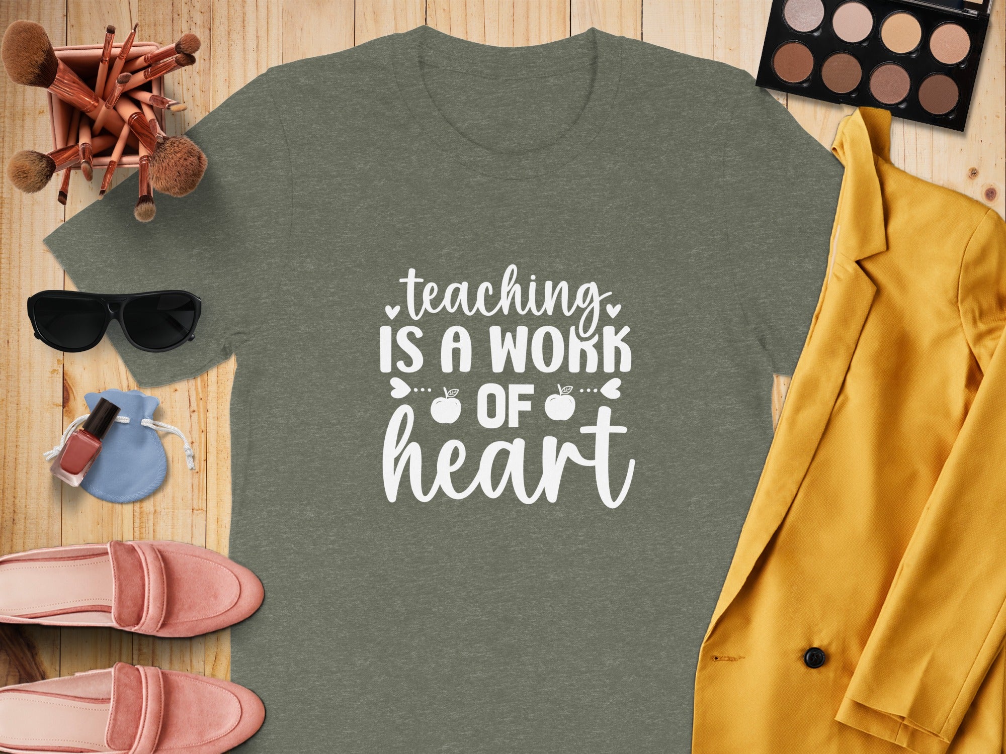 Green t-shirt with white text "teaching IS A WORK OF heart" and surrounding accessories.