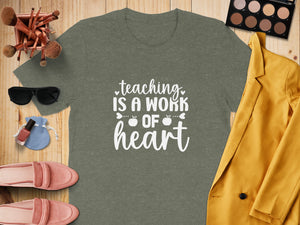 Green t-shirt with white text "teaching IS A WORK OF heart" and surrounding accessories.