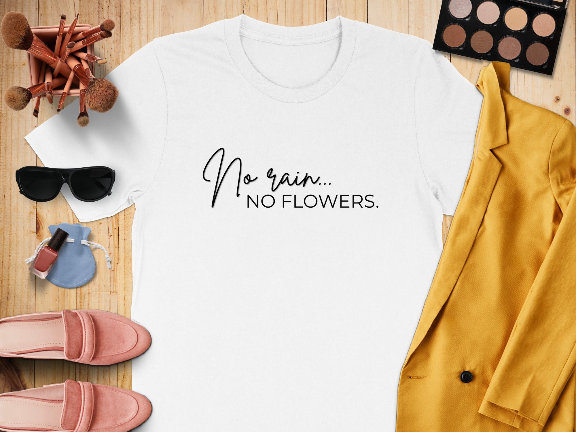 White t-shirt with "No rain... No flowers" text, surrounded by makeup and clothing.