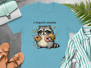 Blue t-shirt with cartoon raccoon holding donuts and hamburger, text "i require snacks."