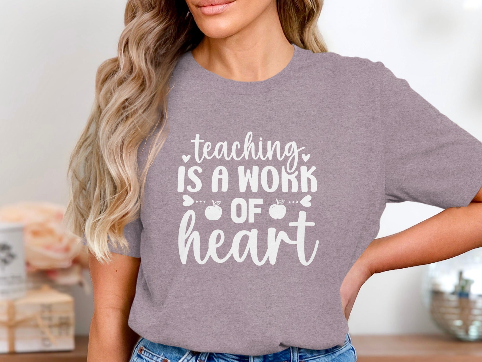 T-shirt with white text: "teaching IS A WORK OF heart" with apple accents.