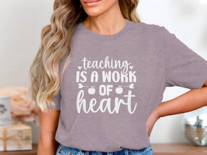 T-shirt with white text: "teaching IS A WORK OF heart" with apple accents.