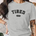 Grey t-shirt with black text "TIRED 24/7" and a butterfly tattoo.