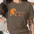 Pie-shaped Pac-Man character chases terrified cartoon turkeys across a t-shirt.