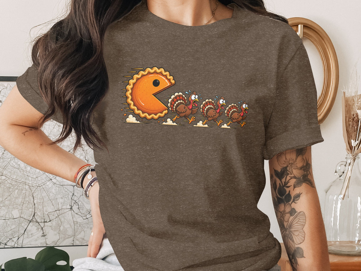 Pie-shaped Pac-Man character chases terrified cartoon turkeys across a t-shirt.