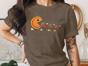 Pie-shaped Pac-Man character chases terrified cartoon turkeys across a t-shirt.
