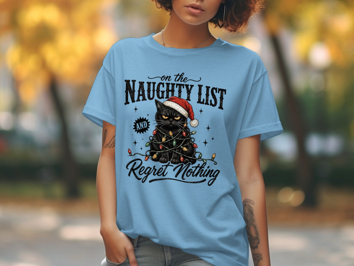 A person wears a light blue t-shirt featuring a black cat tangled in holiday lights with a Santa hat and the text "on the NAUGHTY LIST AND Regret Nothing".