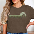 Brown t-shirt with a retro sunset and pine trees graphic design.
