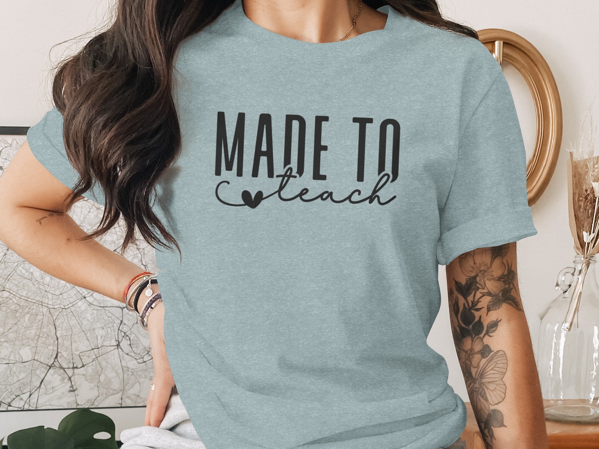 Light blue t-shirt with black text reading "MADE TO teach" and a small heart.
