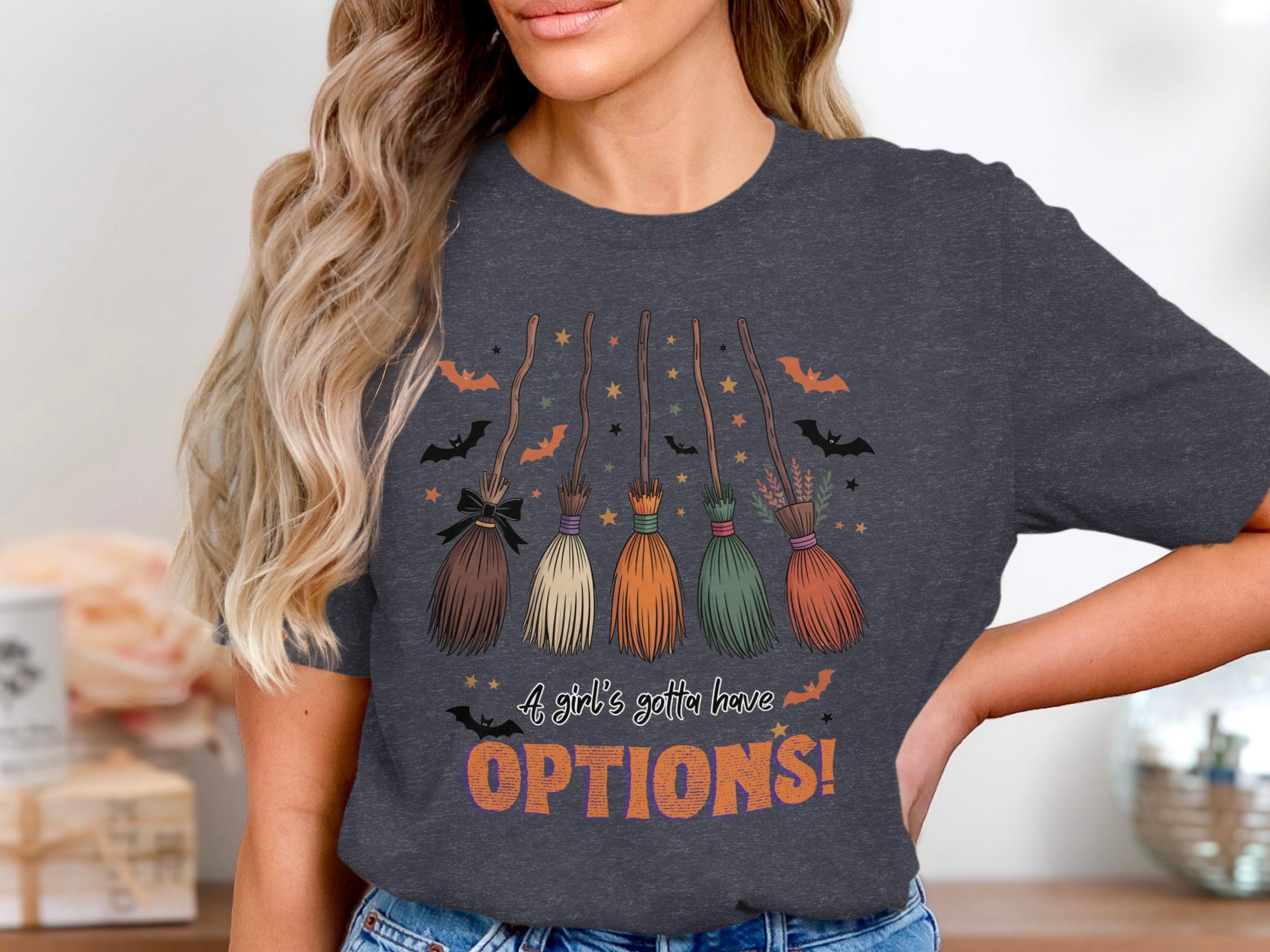 Dark grey t-shirt features five decorative brooms, stars, bats, and text saying "A girl's gotta have OPTIONS!".