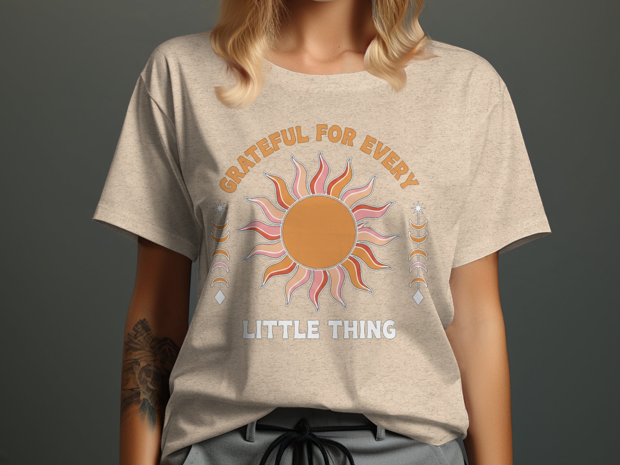 "GRATEFUL FOR EVERY LITTLE THING" text on a beige t-shirt with sun graphic.