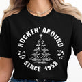 Black t-shirt with white text "Rockin' Around Since 1958" and a Christmas tree graphic.