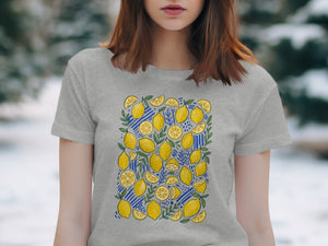Grey t-shirt with a repeating pattern of lemons and green leaves on a blue striped background.