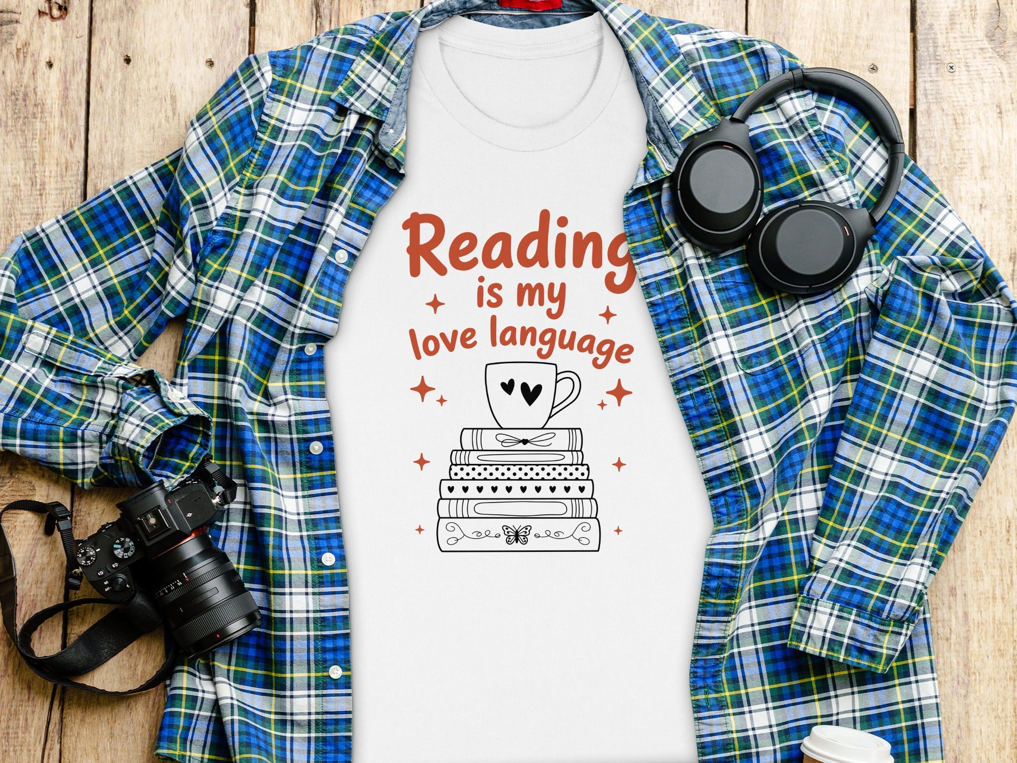 White t-shirt with "Reading is my love language" text, stack of books, cup, and headphones.