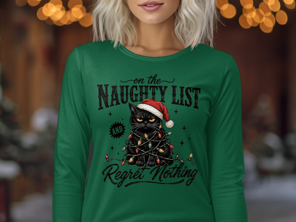 A woman wearing a green long-sleeved shirt with a black cat wearing a Santa hat wrapped in Christmas lights and the text on the Naughty List and Regret Nothing.