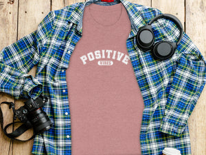 Pink t-shirt with "POSITIVE VIBES" text, plaid shirt, headphones, and camera.
