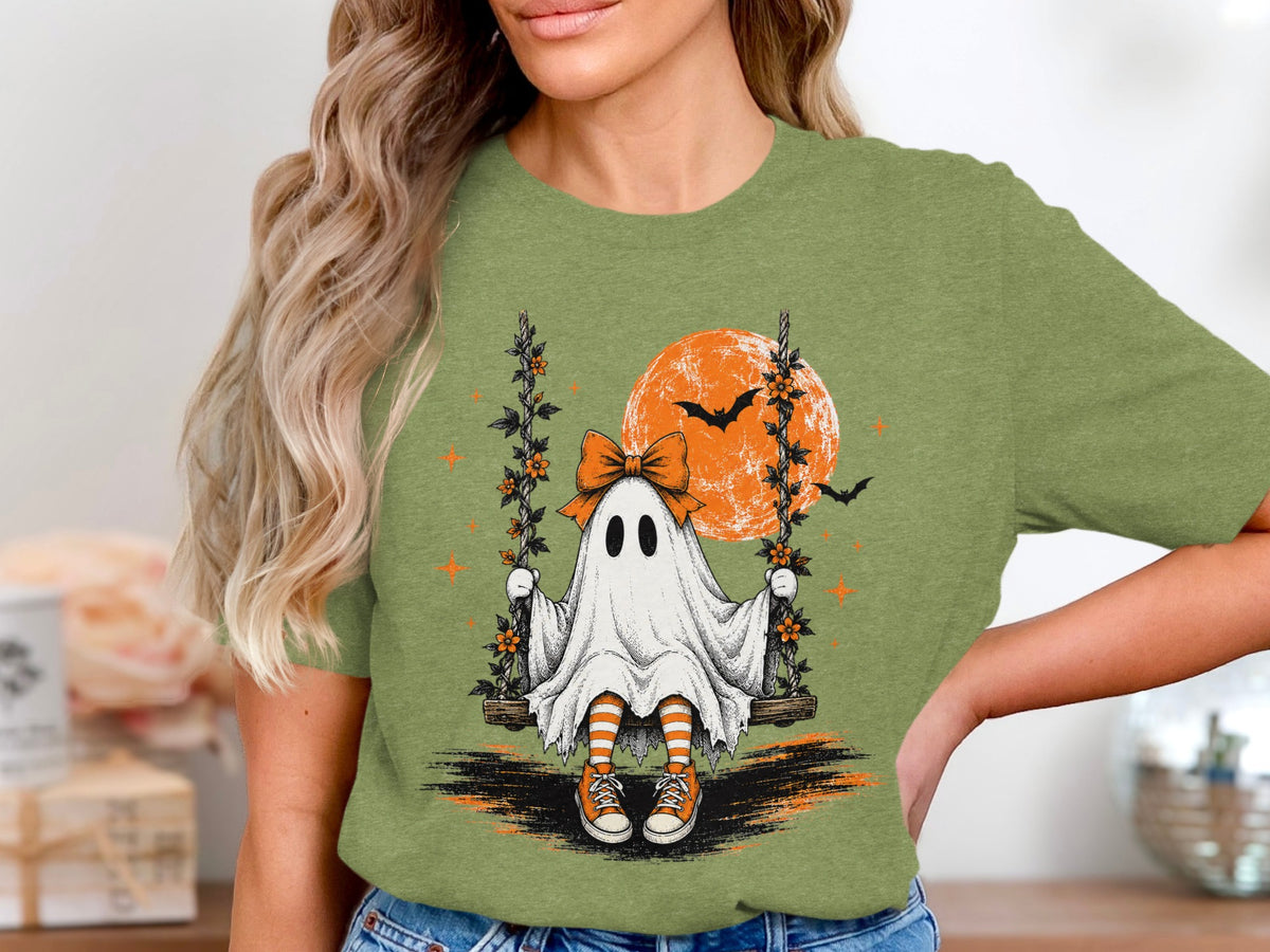 Ghost on a swing with orange moon and bats on Halloween-themed shirt.