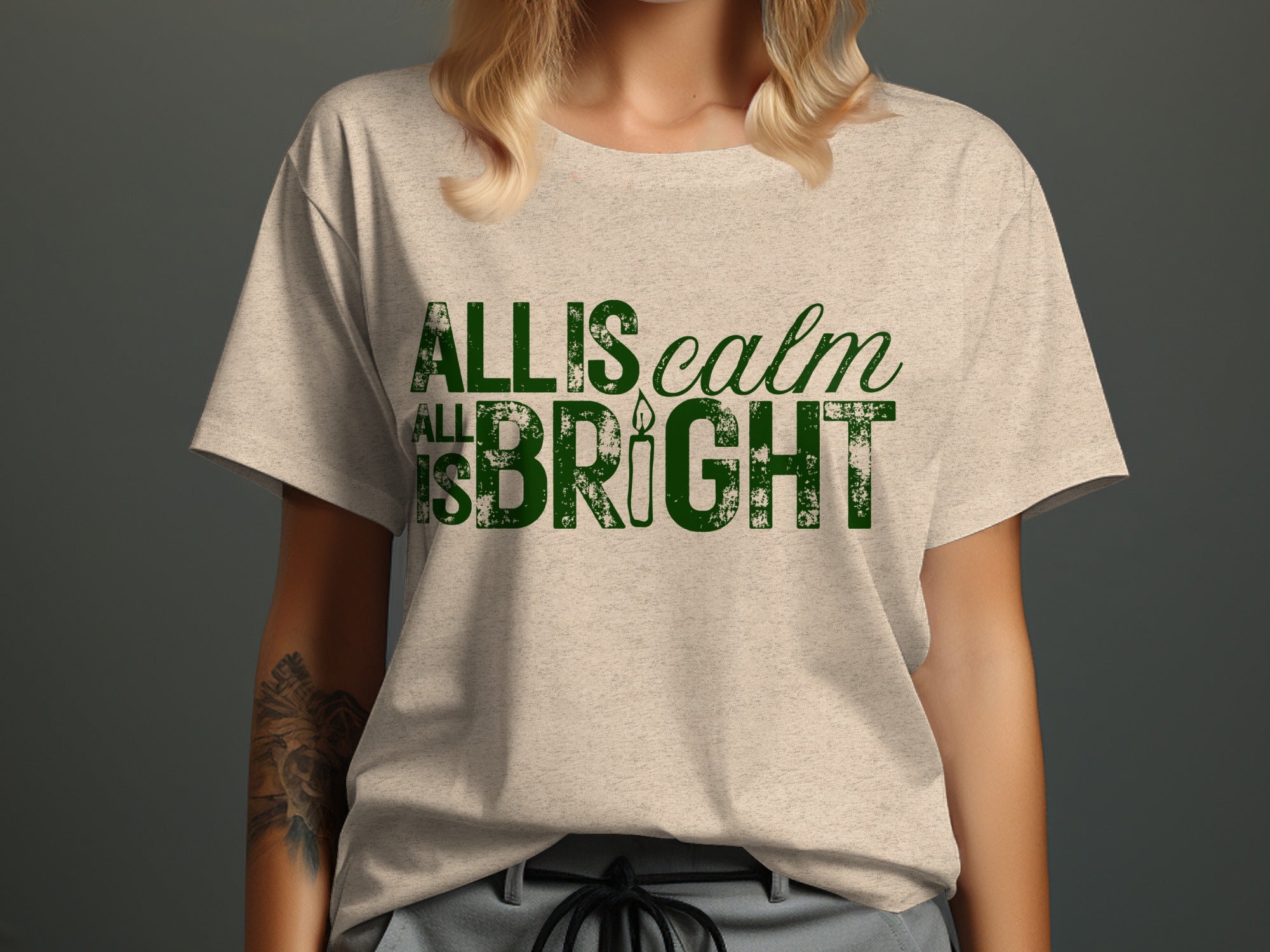 Light-colored t-shirt with green distressed text "ALL IS calm" and "ALL IS BRIGHT" with a candle.