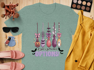 Teal t-shirt with Halloween brooms: pumpkin, spiderweb, bats, ghosts. Text reads "A girl's gotta have OPTIONS!".