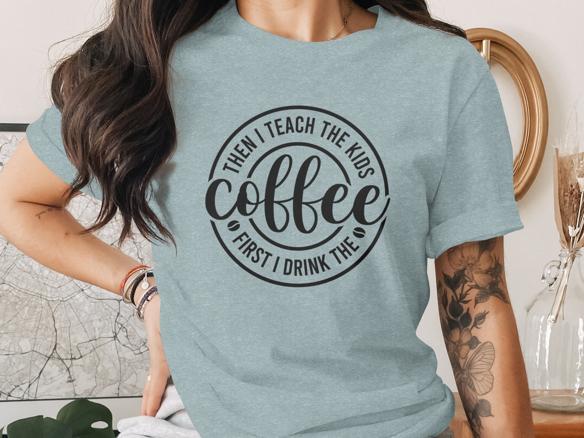Light blue t-shirt with black circular text: "First I drink the coffee, then I teach the kids."