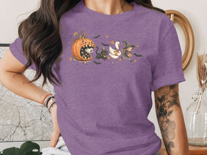 Halloween graphic with grinning pumpkin, ghosts, black cat, witch, and duck on purple shirt.