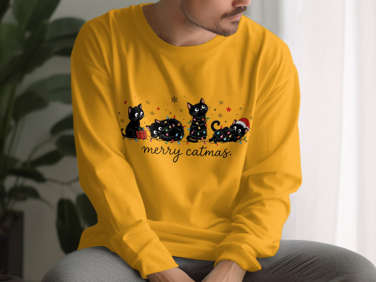 A person wearing a yellow long-sleeve shirt with an illustration of four black cats and the text "merry catmas".