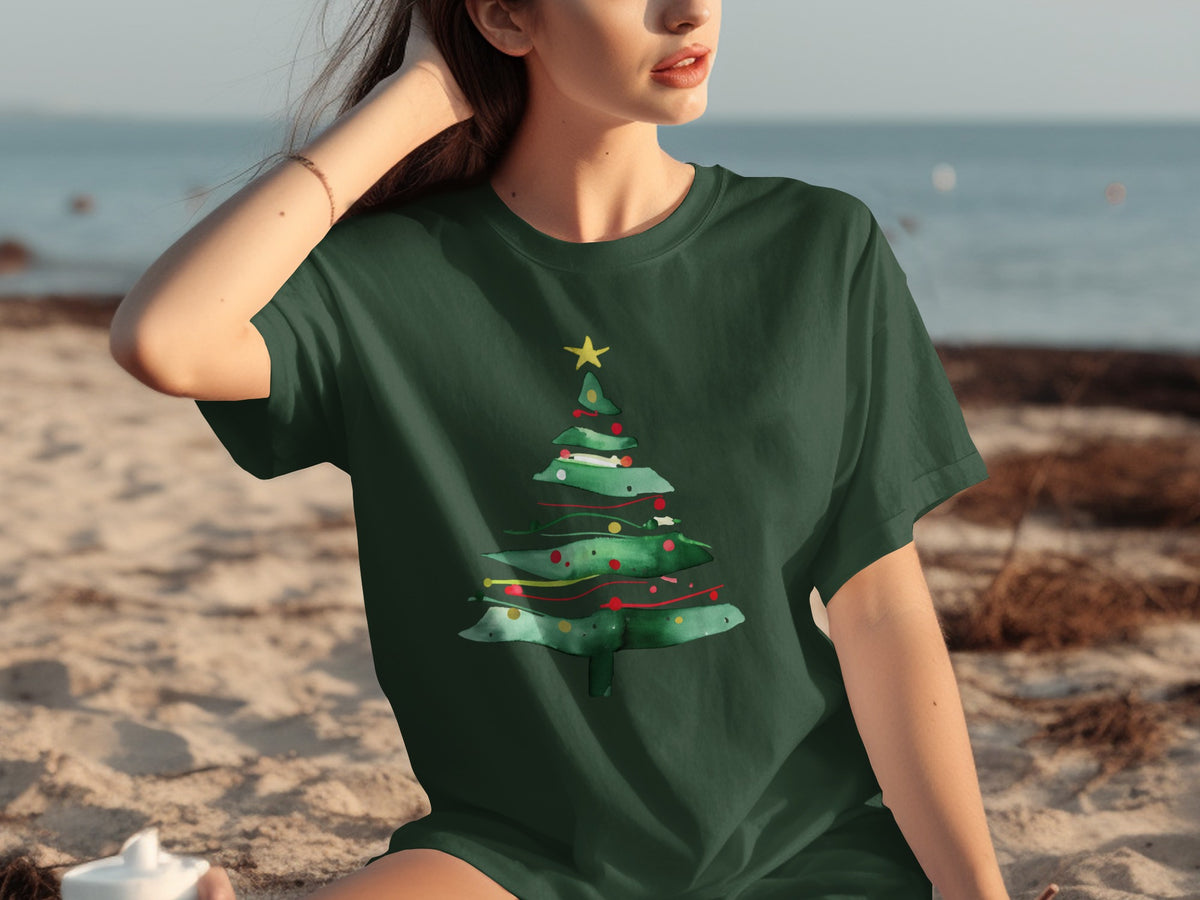 Green t-shirt with watercolor Christmas tree design on a beach.