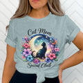 Light blue t-shirt with cat, moon, stars, and floral design reading "Cat Mom Social Club".