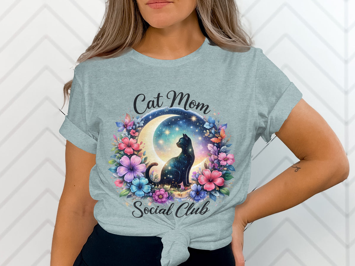 Light blue t-shirt with cat, moon, stars, and floral design reading "Cat Mom Social Club".