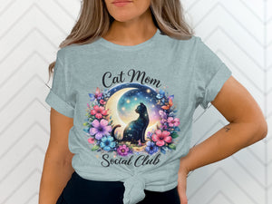 Light blue t-shirt with cat, moon, stars, and floral design reading "Cat Mom Social Club".