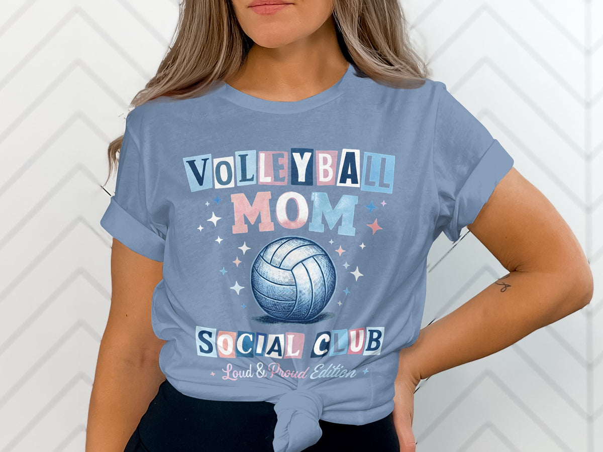 A woman wears a light blue t-shirt with a volleyball graphic and text reading Volleyball Mom Social Club.
